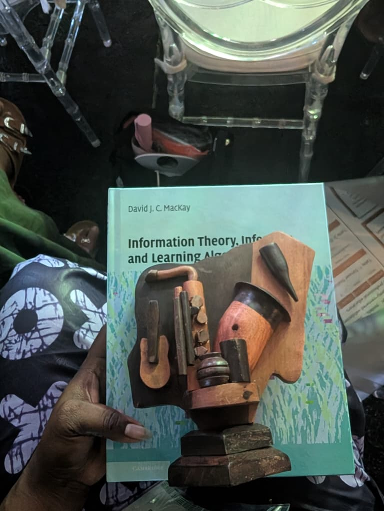 Close-up of the Deep Learning Indaba 2026 award: a signed Cambridge book and handcrafted Nigerian wooden trophy