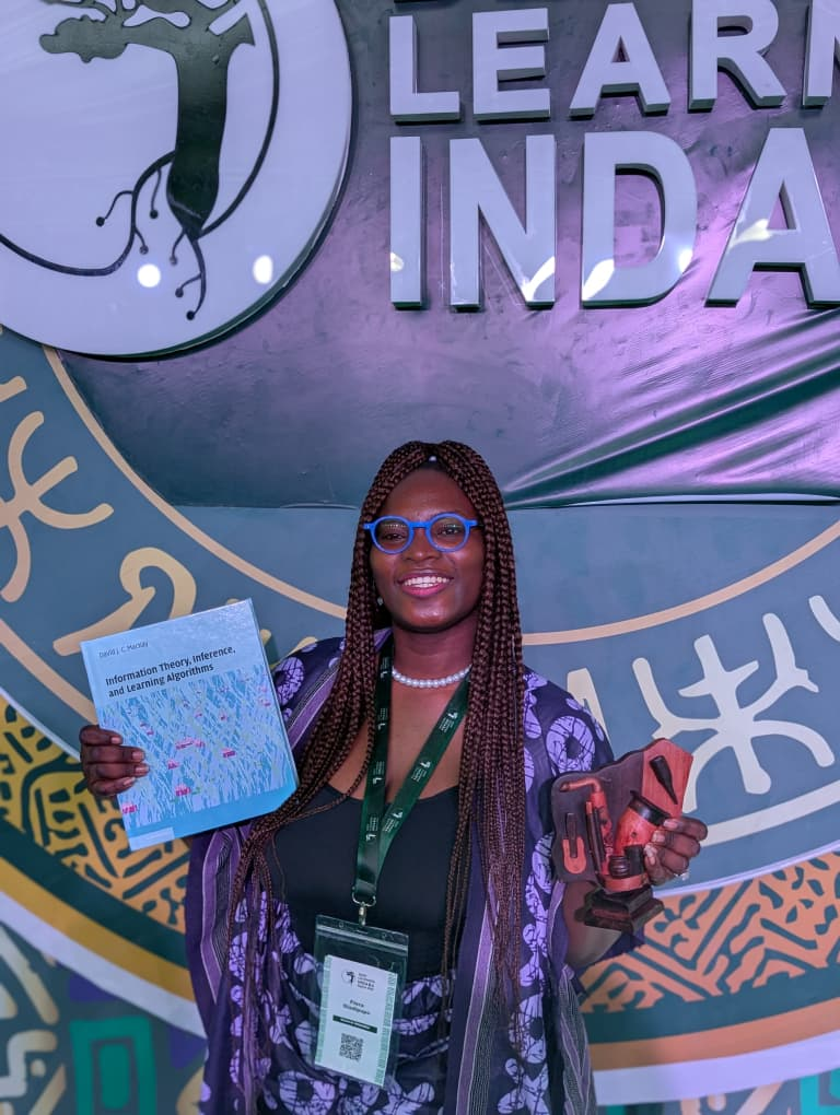 Flora Oladipupo at Deep Learning Indaba 2026 holding the Top 50 Poster Award book and trophy